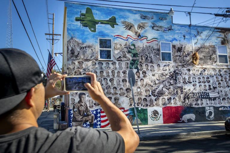 Man uses cell phone to photograph a mural with Mexican and American flags