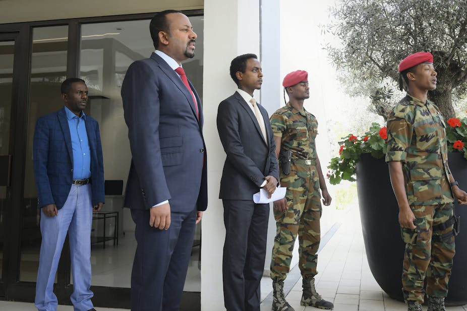 Prime Minister of Ethiopia Abiy Ahmed stands at the entrance to a building, withtwo soldiers and two other men