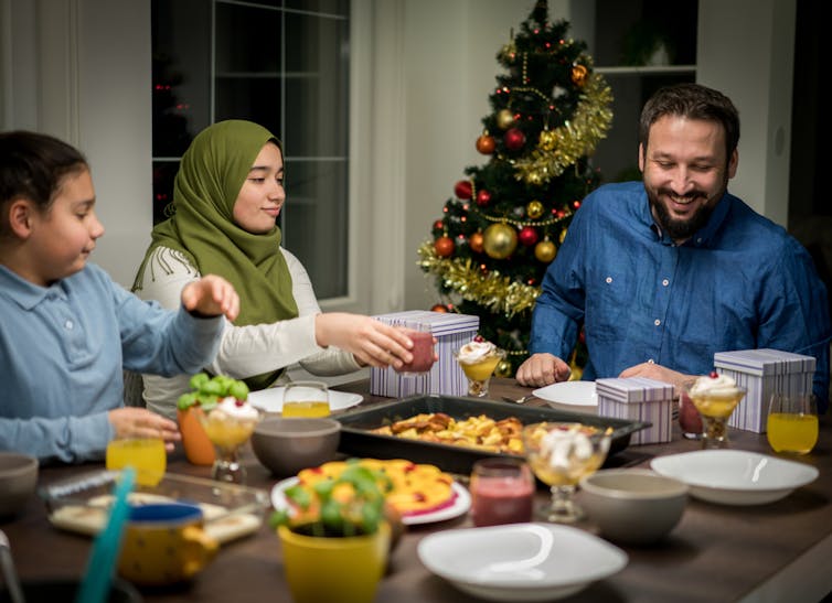 Interfaith family sat having dinner with Christmas tree in the background