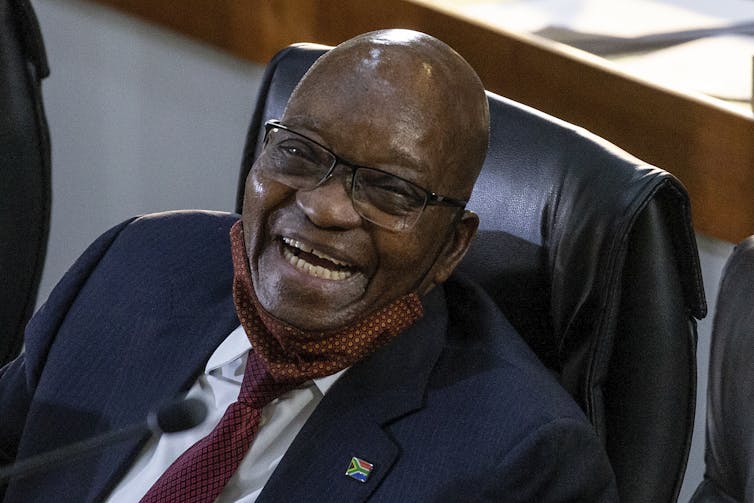 Jacob Zuma, spotting shaven head, specs, and a brown Covid-19 mask below the mouth, laughs heartily