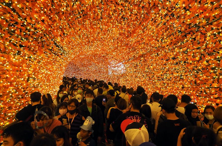 A large crowd of people walks through an orange tunnel.