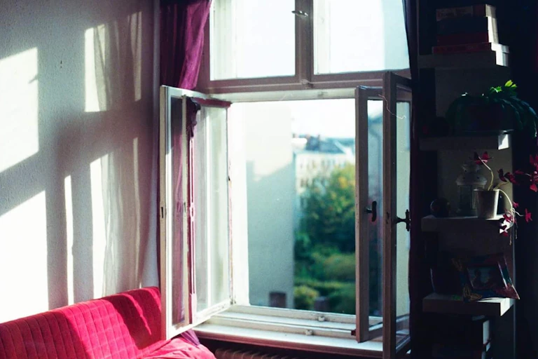 An open window next to a red couch.