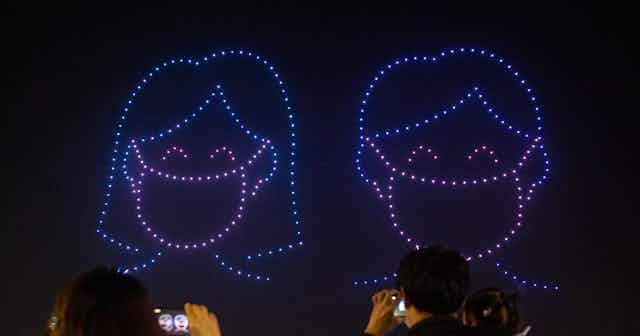 Drones form a picture in the night sky of a woman and a man wearing masks.