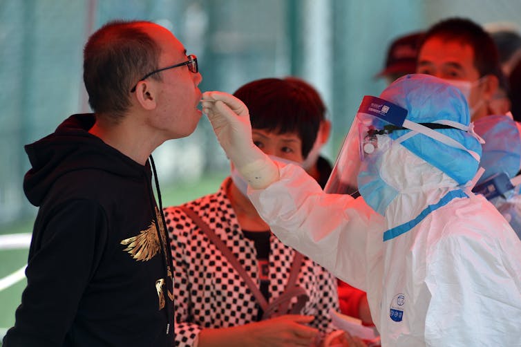 A health worker in full personal protective equipment adminsters a coronavirus test.