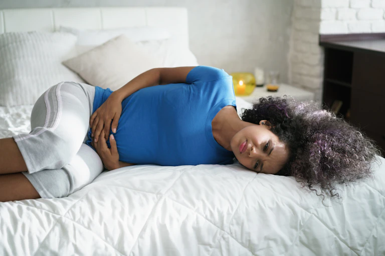teenage girl lying on bed holding her perlvis.