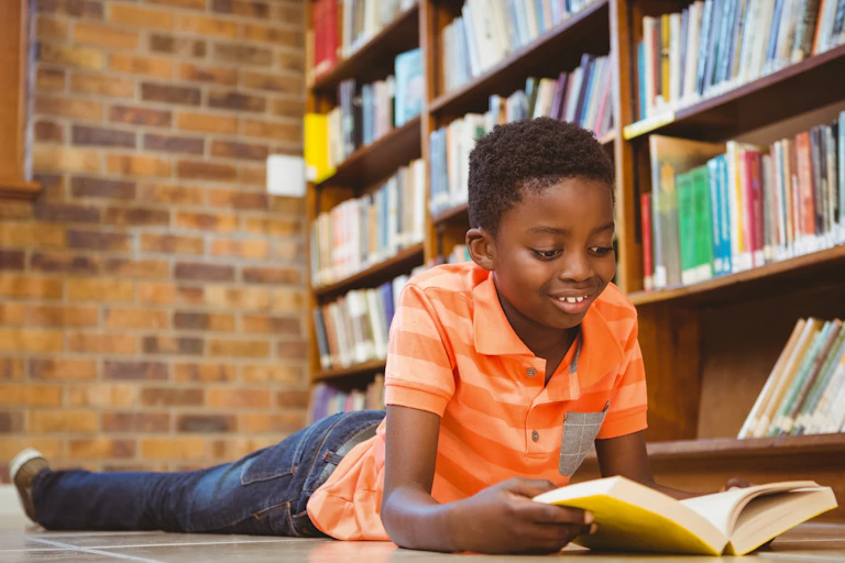 Child reads a book on the floor of a library.
