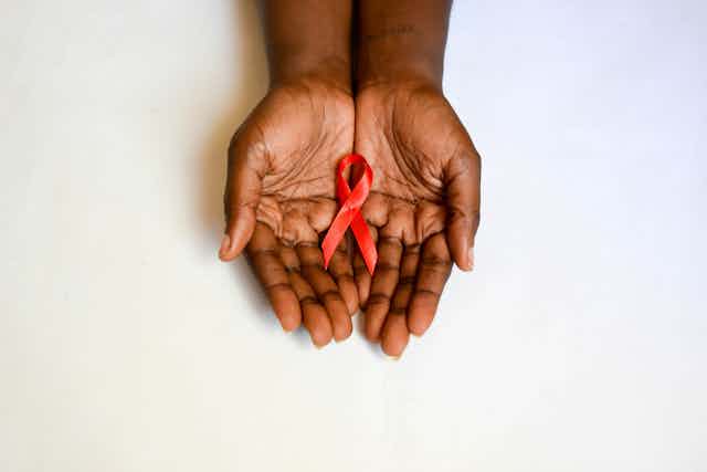 Two hands hold a red ribbon in their palms against a white backdrop.