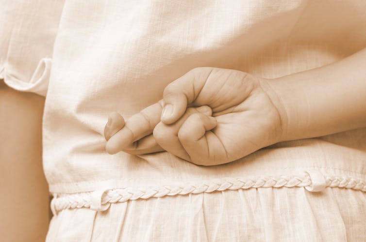 Close up of female kid hand crossing fingers behind her back