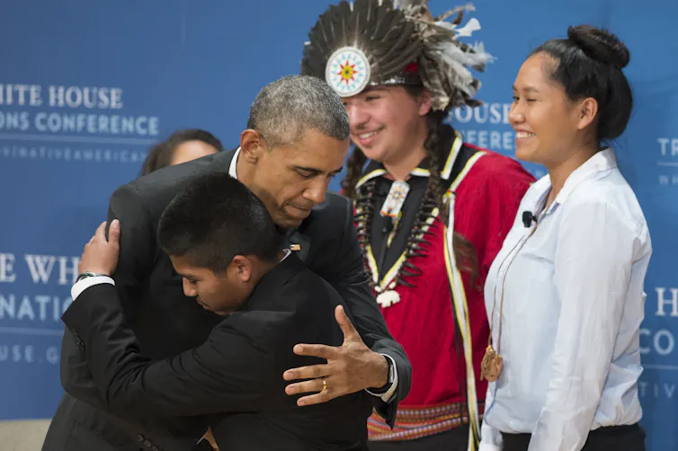 Barack Obama hugs Philip Douglas of the Seminole Nation of Oklahoma, in front of Brayden White of St. Regis Mohawk Tribe and Blossom Johnson of the Navajo Nation; at the 2015 White House Tribal Nations Conference