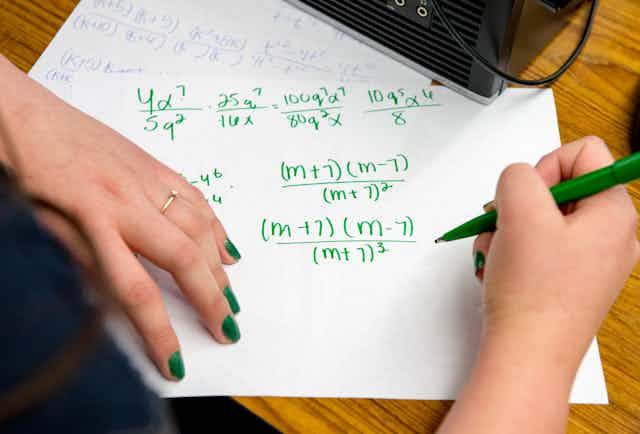 Young woman's hands shown completing an algebra problem in green ink