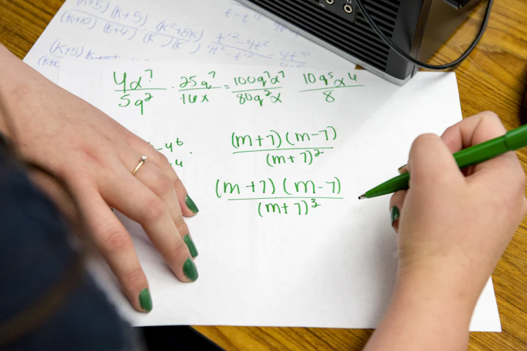 Young woman's hands shown completing an algebra problem in green ink