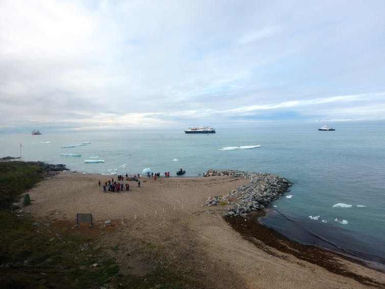 Ships anchored offshore in icy water with small group of passengers standing on a point of land.