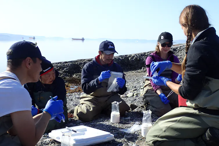 A group of people sit on shore learning to use sampling equipment.