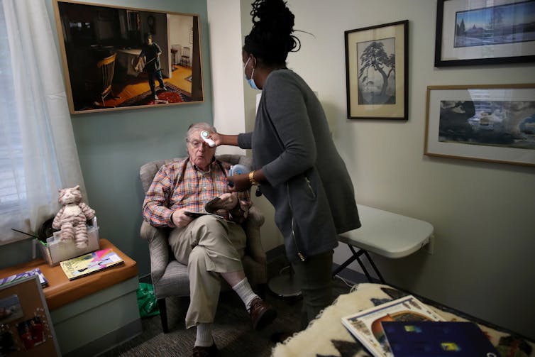 An assisted care facility staff member checks a resident's temperature