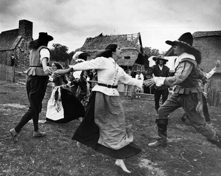 Women and men in period clothing hold hands as they dance in a circle.