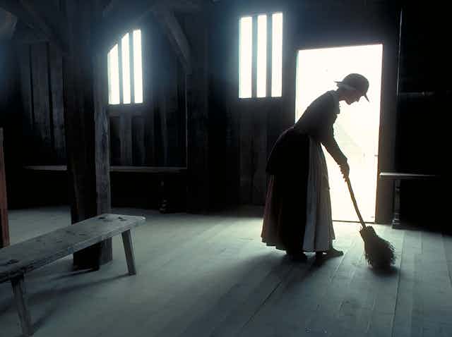 A historical re-enactor sweeps an empty house at Plymouth Plantation.
