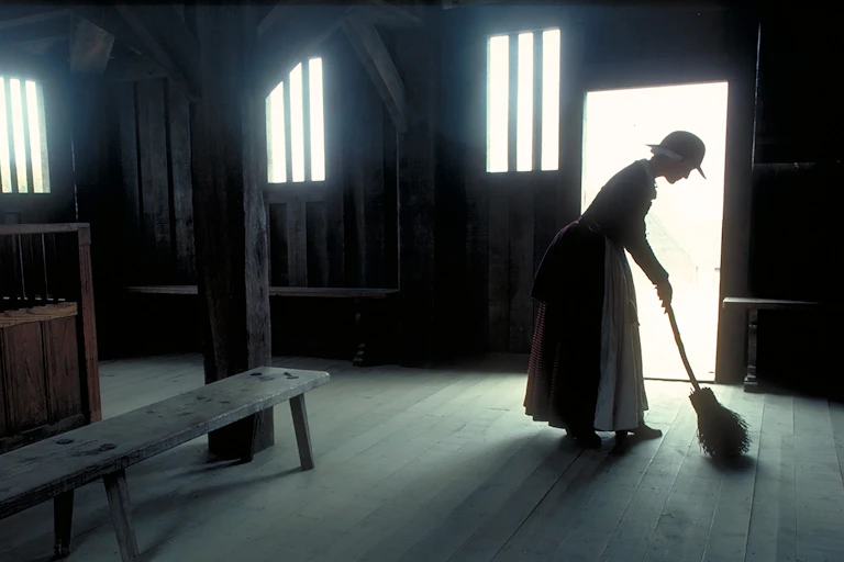 A historical re-enactor sweeps an empty house at Plymouth Plantation.