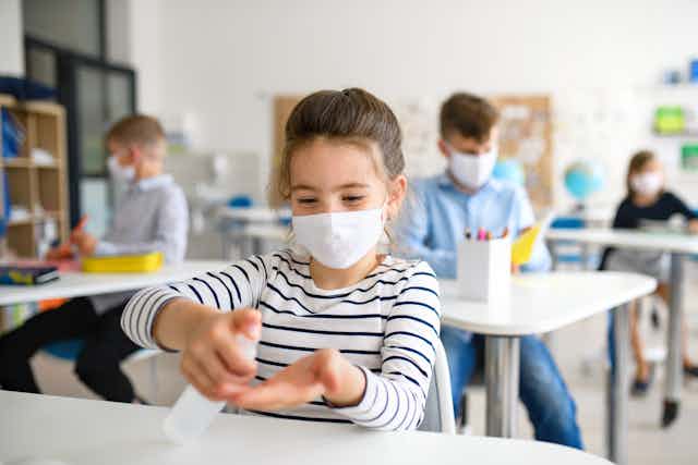 Girl wearing mask in class, and putting on hand sanitiser.