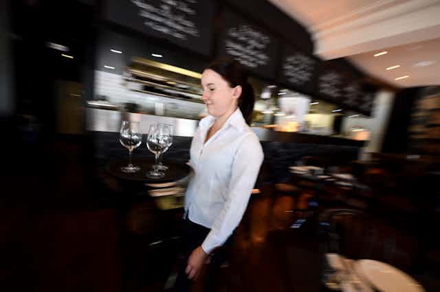 A waitress, carrying three empty wine glasses, walking through a restaurant