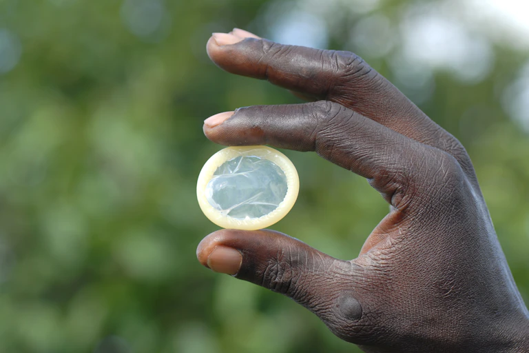 A hand holding a condom between thumb and forefinger