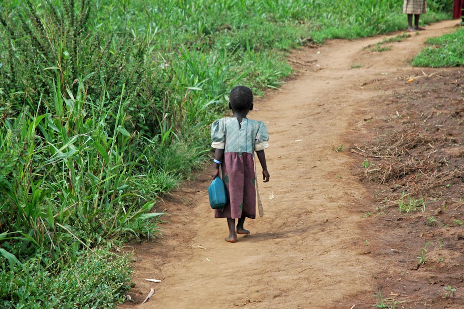 Unidentified little girl carries a jerry-can down a dirt pathway.