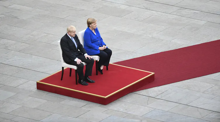 Boris Johnson and Angela Merkel sitting on a podium.