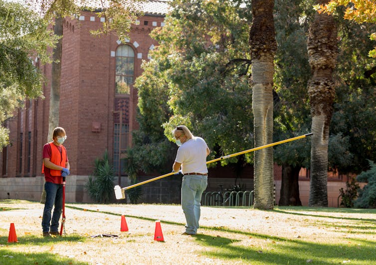 Two technicians take wastewater sample via a manhole.