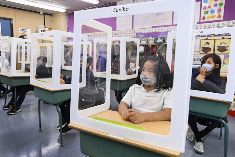 Children wearing masks behind screens in a classroom.