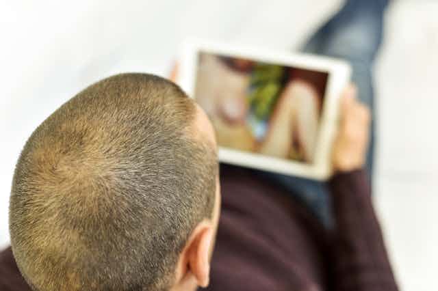 Hombre con el pelo rapado viendo a una mujer desnuda en una pantalla.