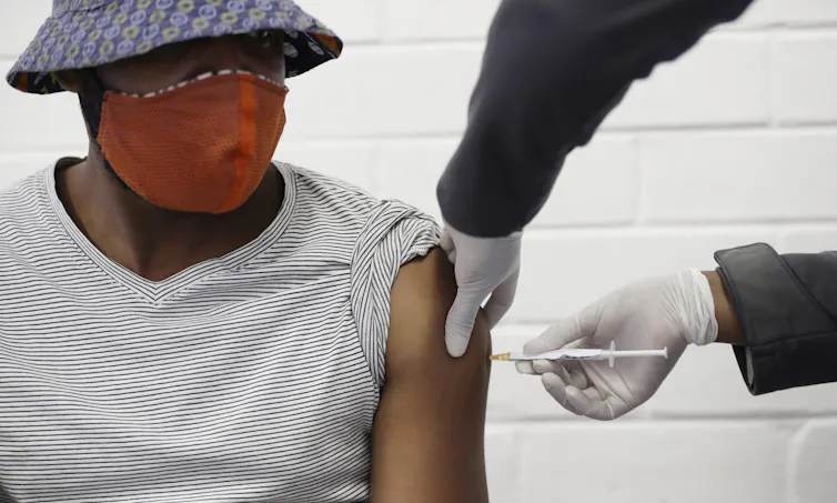 A man wearing a hat and a face mask gets an inject from a health-care worker out of frame.