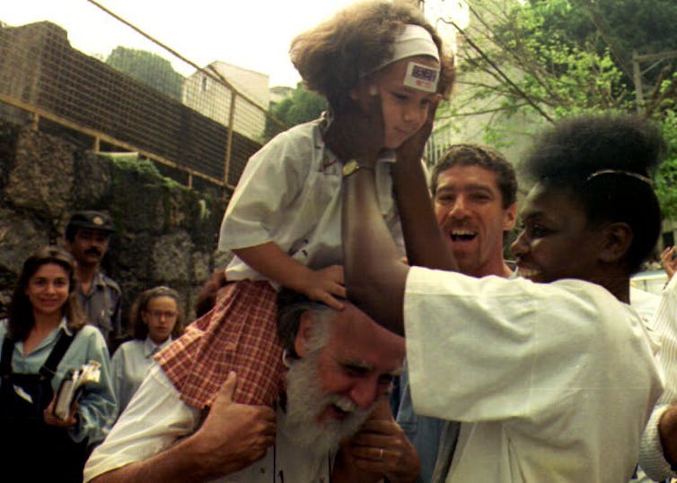 Silva, a black woman, holds up a smiling young child as a crowd looks on