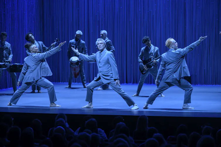 Byrne and two dancers bathed in blue light.