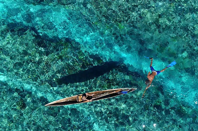 Person swimming in ocean with canoe.