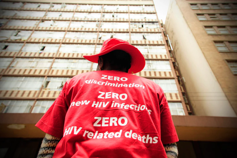 A woman wearing a t-shirt with slogans stands in front of a building.