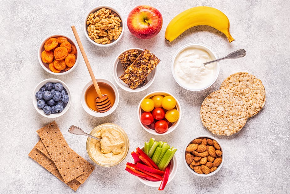 A spread of healthy snacks, including dried apricots, a banana, walnuts, almonds, and oat cakes.