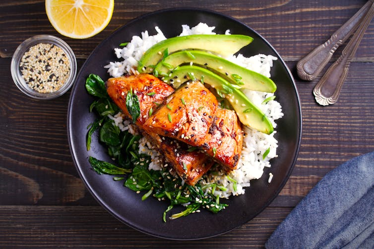 A plate of cooked salmon with rice and avocado.