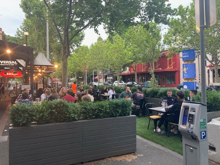 Diners sit within a green parklet on Lygon Street in Melbourne, having fun on reclaimed street space.