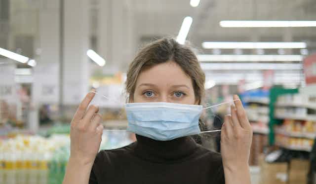 A young woman puts on a face mask in a supermarket.