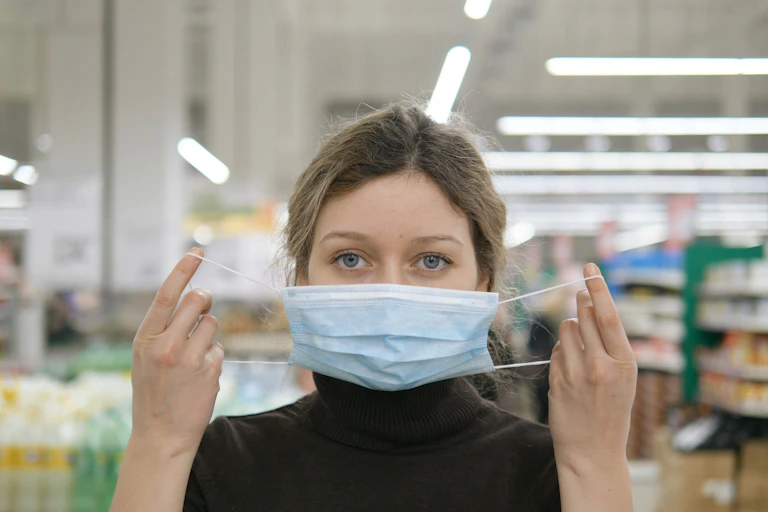 A young woman puts on a face mask in a supermarket.
