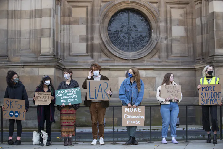Young people hold placards in front of grand building.