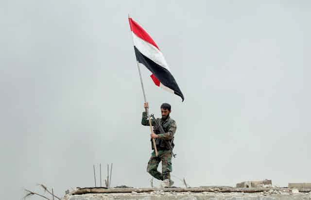 Syrian soldier planting a national flag after regime forces retake a suburb of Damascus, May 2018.