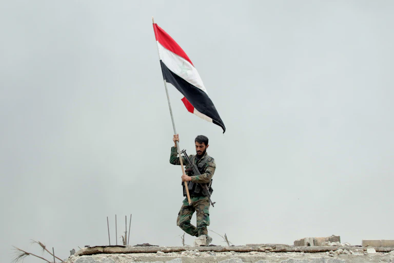 Syrian soldier planting a national flag after regime forces retake a suburb of Damascus, May 2018.