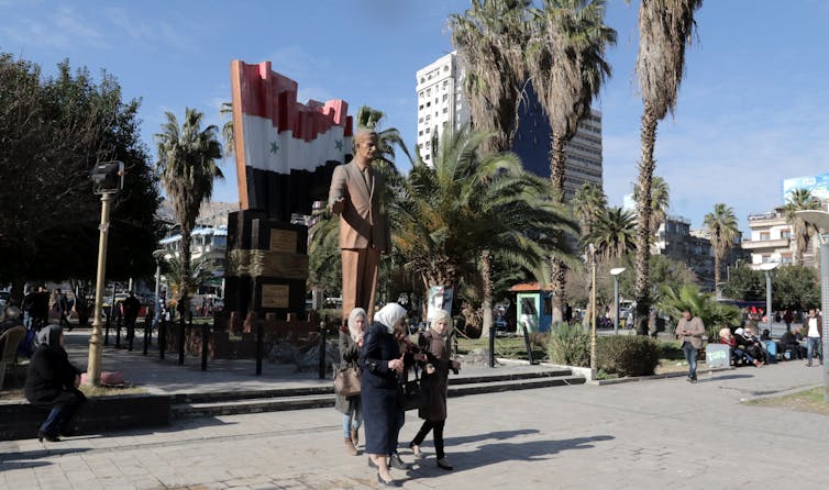 Women walk past a statue of former Syrian president Hafez al-Assad in Damascus.