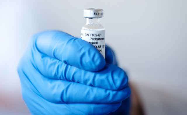 A hand holding a vial of COVID vaccine.