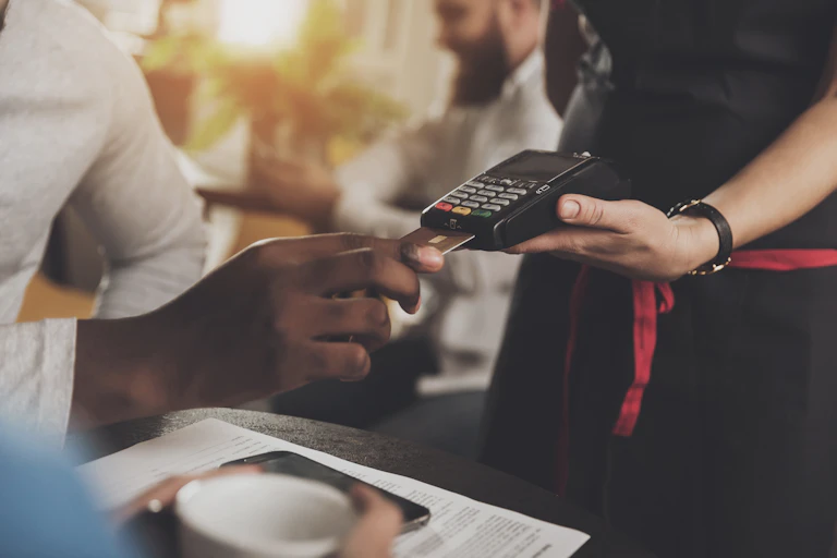 A Black customer inserts a credit card into a point of sale device held by a white waiter.
