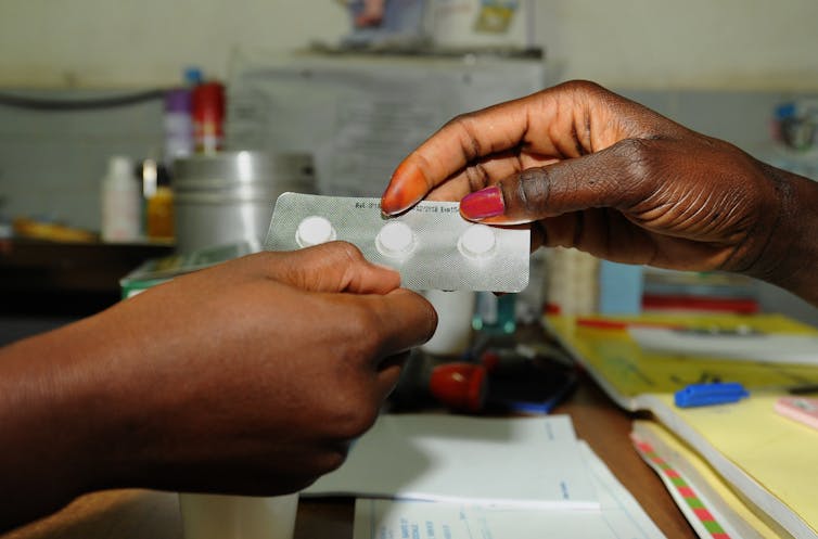 A close-up picture of one person handing a sheet of pills to another.