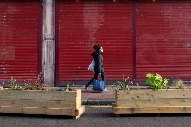 A woman walks past a shuttered building carrying shopping.