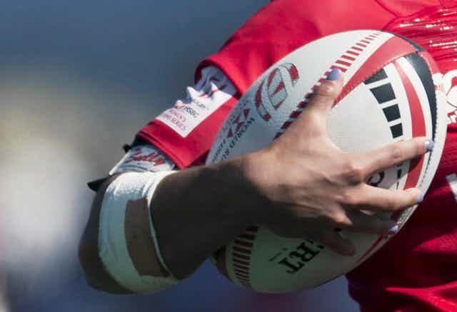 A closeup of a woman holding a rugby ball in her arm.