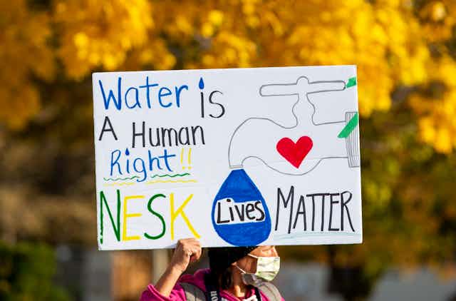 A person holding a sign that reads: Water is a human right. Nesk lives matter.