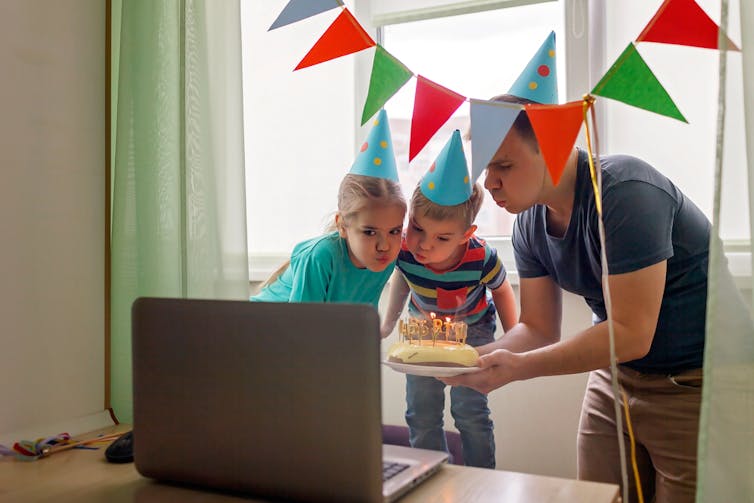 Father holding birthday cake in front of computer screen with children for a Zoom birthday party